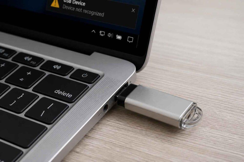 Srebrny pendrive podłączony do portu USB laptopa z komunikatem o nierozpoznanym urządzeniu