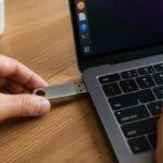 Dłoń podłącza pamięć USB do laptopa na drewnianym biurku