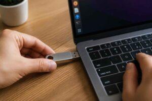 Dłoń podłącza pamięć USB do laptopa na drewnianym biurku