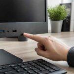 Dłoń wskazuje porty USB na przednim panelu komputera przy biurku