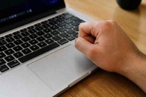 Zaciśnięta pięść nad klawiaturą laptopa na drewnianym biurku