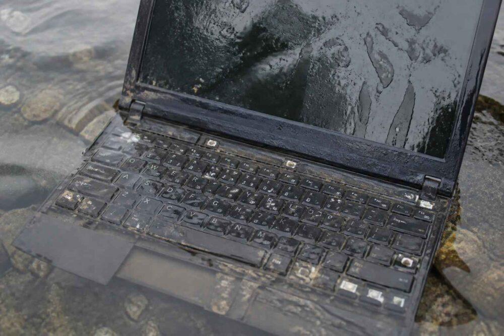 Uszkodzony laptop leżący w wodzie na kamienistej powierzchni